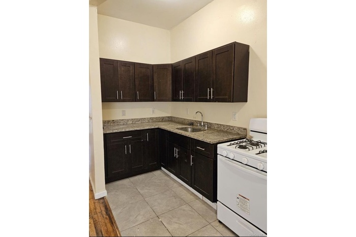 Kitchen featuring gas range gas stove, dark brown cabinets, light stone counters, and light wood finished floors
