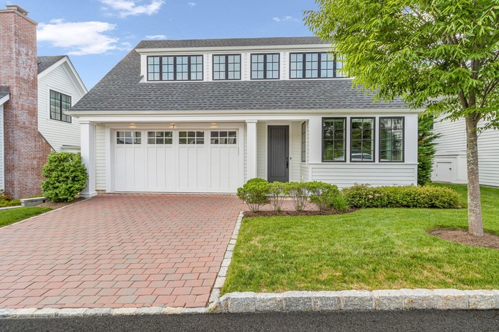 View of front of home featuring decorative driveway, a front lawn, roof with shingles, and a garage