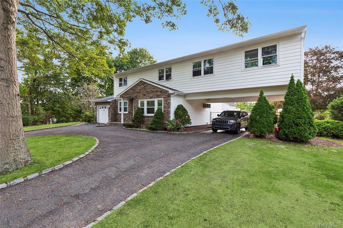 View of front facade featuring driveway, a front yard, a garage, and stone siding