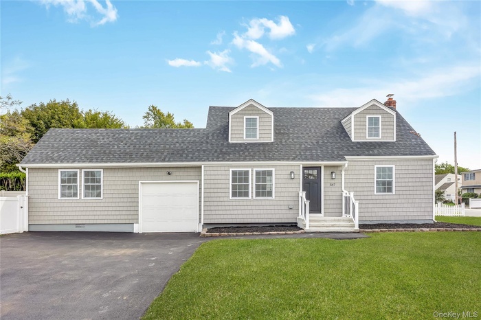 Cape cod house with asphalt driveway, a shingled roof, an attached garage, and a chimney