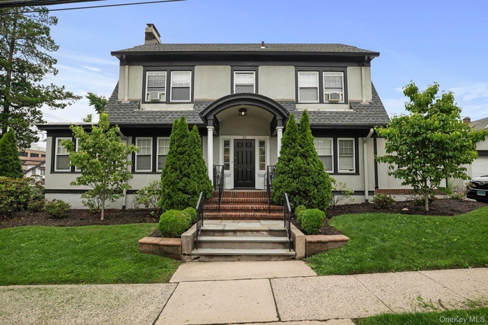 View of front of home with stucco siding, a front lawn, and a shingled roof