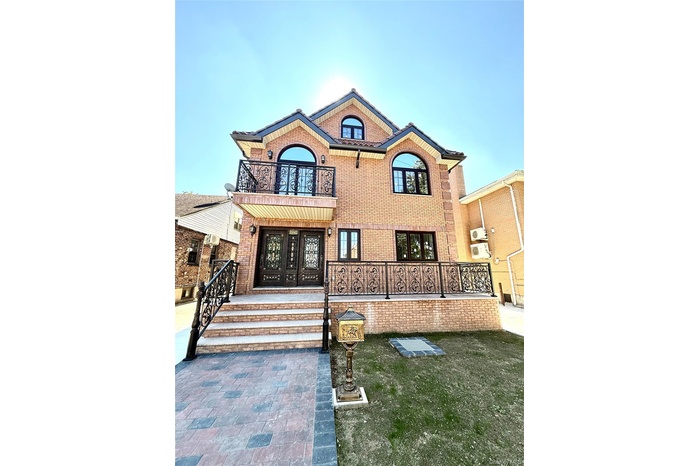 View of front facade with a balcony, brick siding, a front lawn, and a wall unit AC