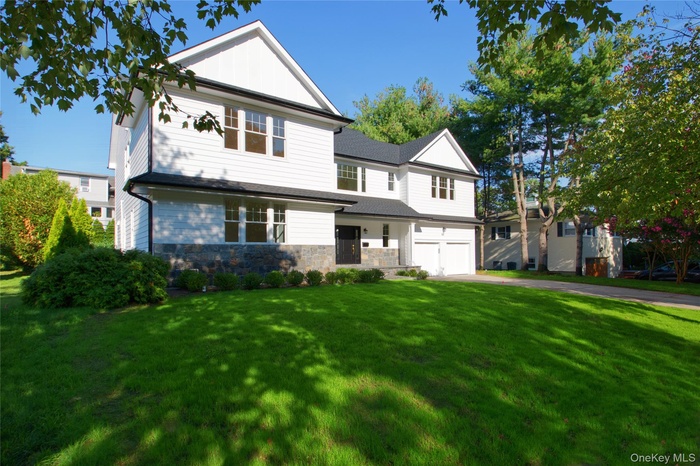 View of front of property with a front lawn, stone siding, an attached garage, driveway, and roof with shingles