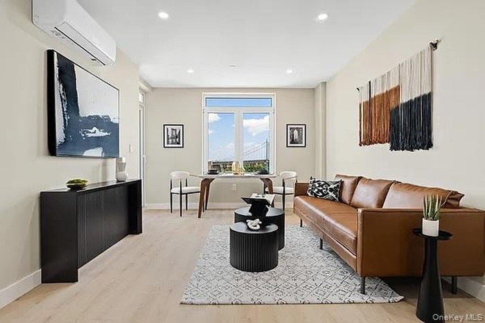 Living area with an AC wall unit, light wood-style floors, and recessed lighting