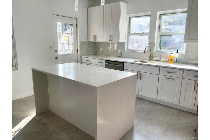 Kitchen with light stone counters, white cabinetry, decorative backsplash, and stainless steel dishwasher