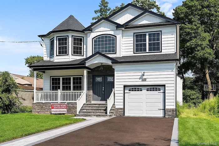 View of front facade with an attached garage, a front yard, stone siding, roof with shingles, and covered porch