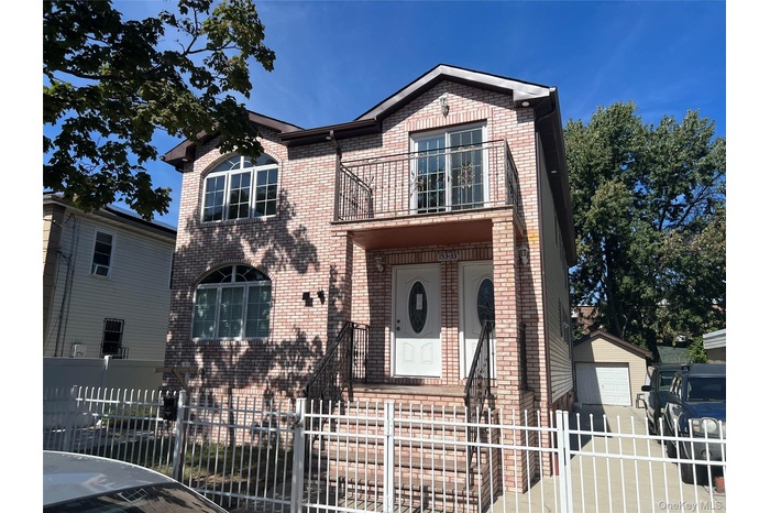 Traditional-style home featuring a fenced front yard, brick siding, a balcony, and a detached garage