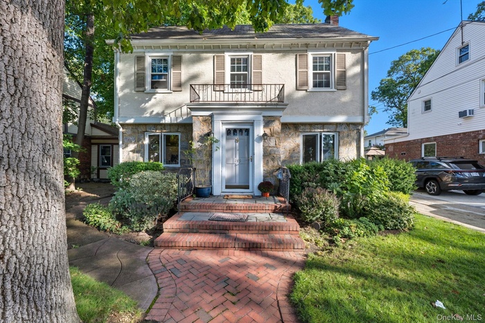 View of front of property featuring a chimney, stucco siding, a balcony, stone siding, and a wall mounted air conditioner