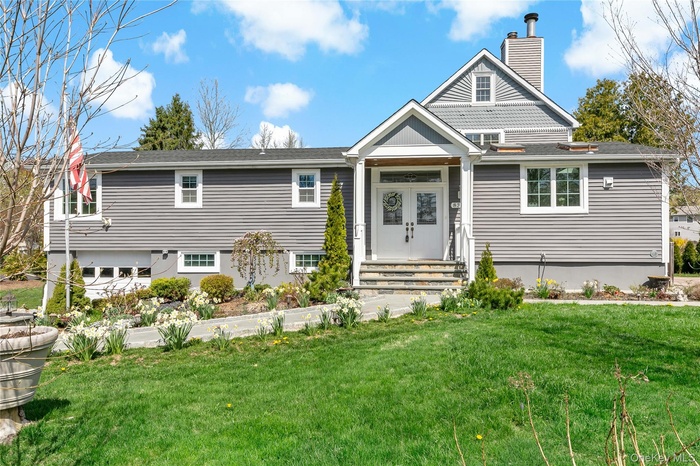 View of front of property with a front yard, a chimney, and a shingled roof