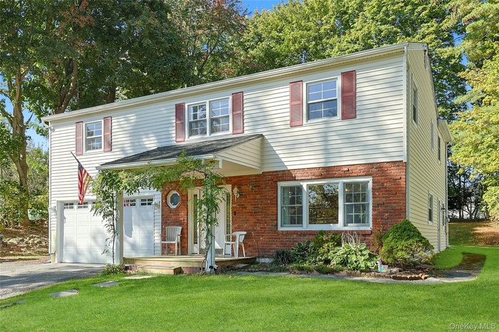 Traditional-style house with brick siding, a front lawn, driveway, and a garage