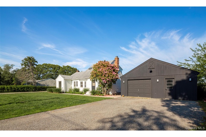 View of front of house featuring a garage, a front lawn, asphalt driveway, a chimney, and an outdoor structure