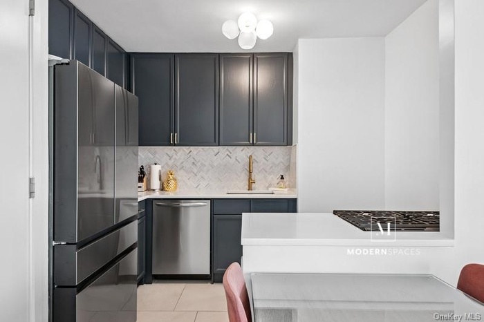 Kitchen featuring appliances with stainless steel finishes, backsplash, light tile patterned flooring, and light stone counters