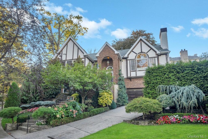 View of front of home featuring brick siding, a chimney, stairway, concrete driveway, and a front yard