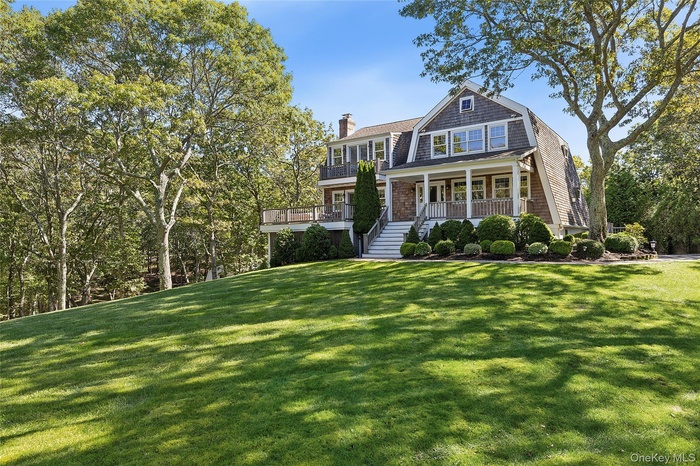 Shingle-style home featuring a gambrel roof, a porch, a front lawn, and a chimney