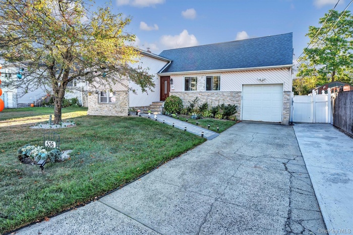 View of front of property featuring concrete driveway, stone siding, a garage, and roof with shingles