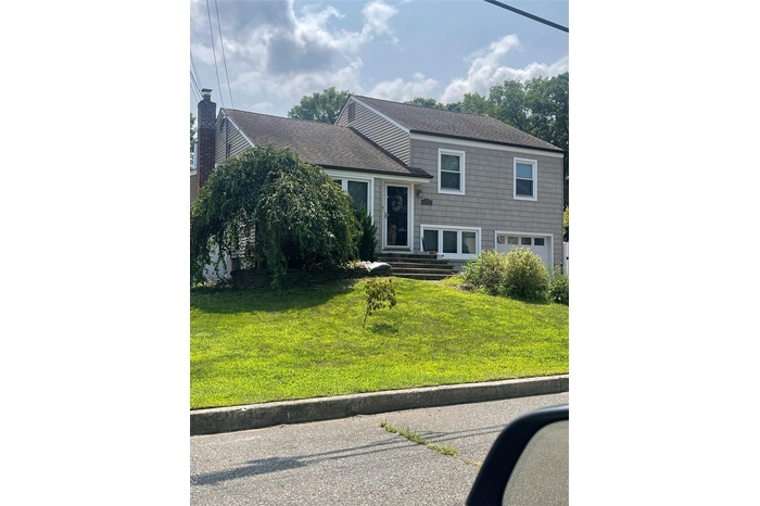 View of front of home with roof with shingles, a front lawn, and a garage
