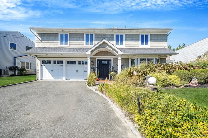 Traditional-style home with covered porch, roof with shingles, driveway, and an attached garage