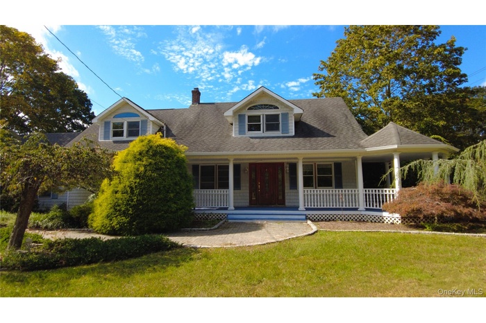View of front of home with covered porch, a chimney, roof with shingles, and a front yard