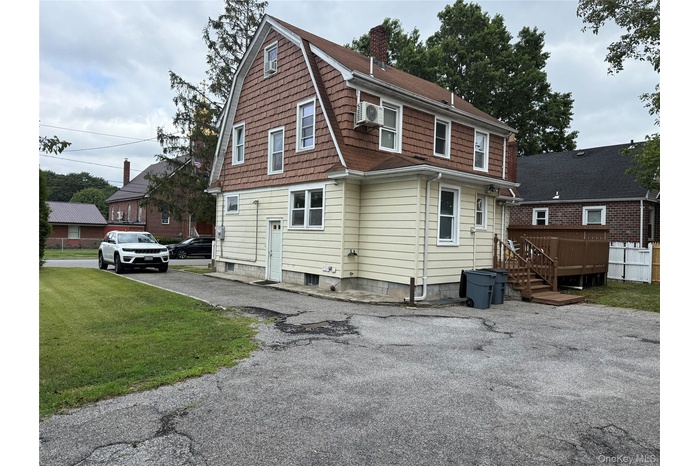 Back of house featuring a chimney, a yard, a gambrel roof, and a deck