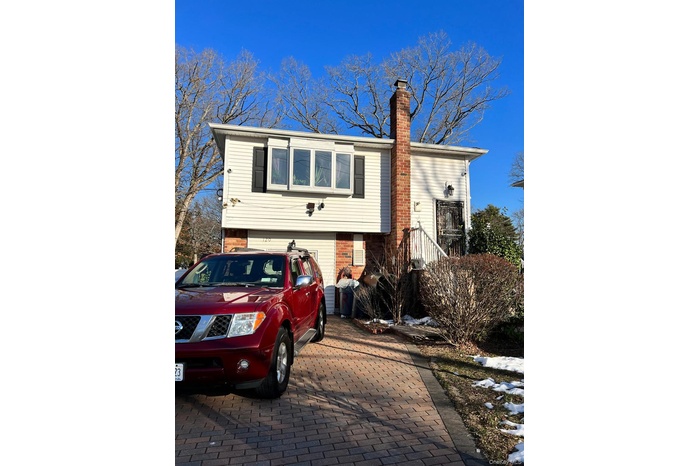 View of front of property featuring a chimney, brick siding, and decorative driveway