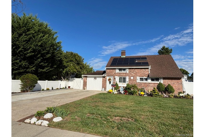 View of front of home featuring a gate, roof mounted solar panels, a chimney, driveway, and brick siding