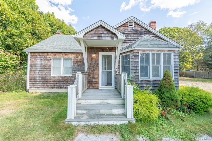 View of front of home featuring a chimney, roof with shingles, a front lawn, and a wooden deck