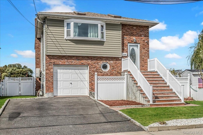 View of front of property featuring driveway, a garage, a gate, and brick siding