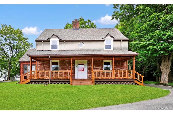 View of front facade featuring a chimney, covered porch, a front yard, and a shingled roof
