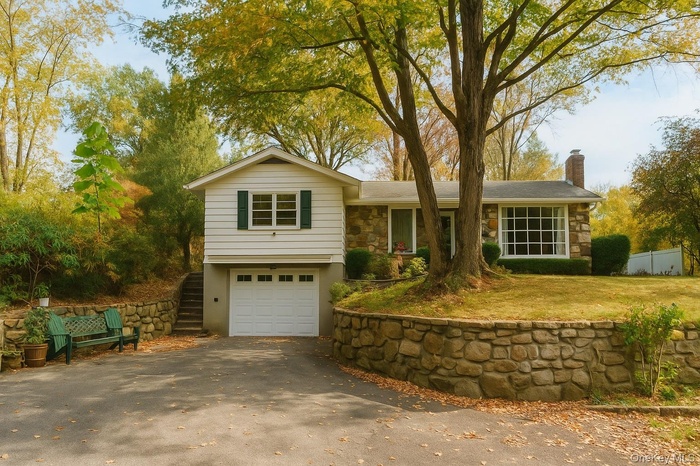 Ranch-style house with stone siding, a chimney, driveway, a garage, and stairway