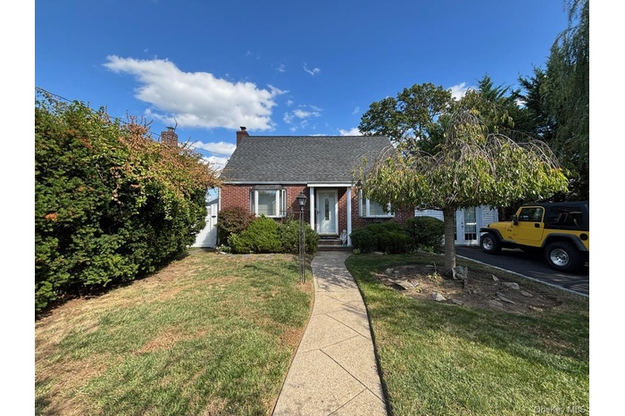 View of front facade featuring brick siding, a front yard, and roof with shingles