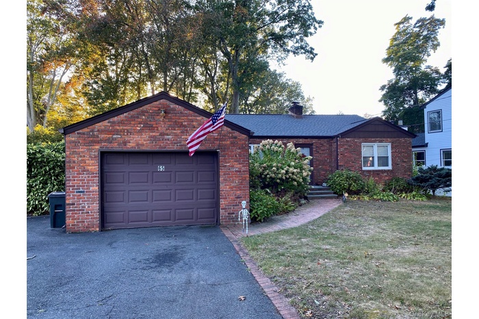 Ranch-style home featuring a front lawn, a chimney, brick siding, a garage, and asphalt driveway