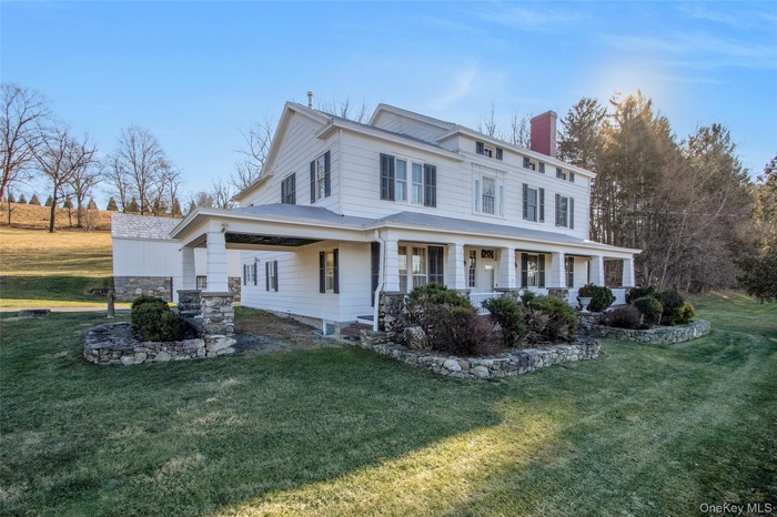 View of front facade featuring a chimney, covered porch, and a front lawn
