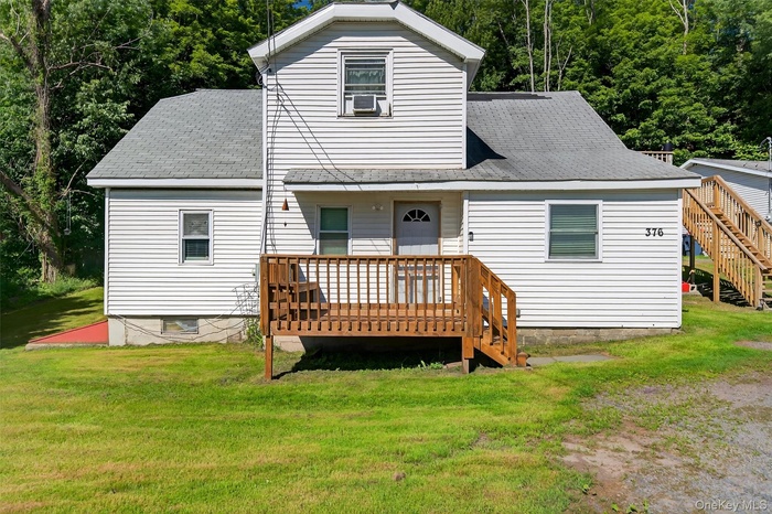 Back of house with a deck, a lawn, stairway, and a shingled roof