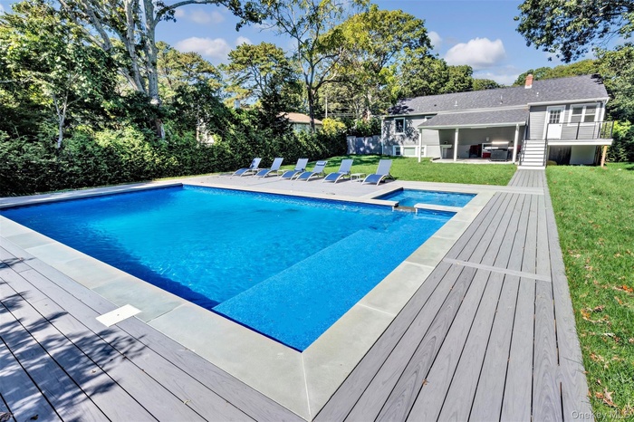 View of swimming pool featuring a patio area, a lawn, a pool with connected hot tub, view of scattered trees, and stairway