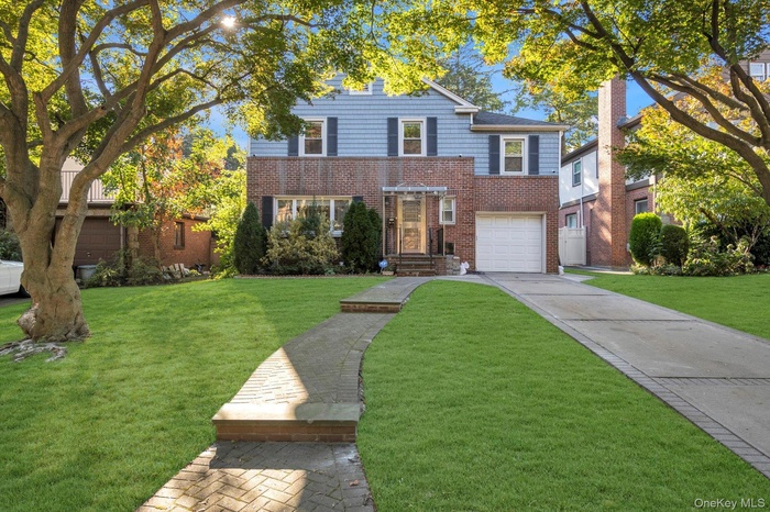 Traditional-style house with brick siding, driveway, a front yard, and an attached garage