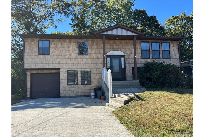 Raised ranch featuring a front yard, concrete driveway, and an attached garage