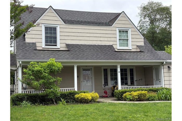 View of front facade with a porch, a shingled roof, and a front yard