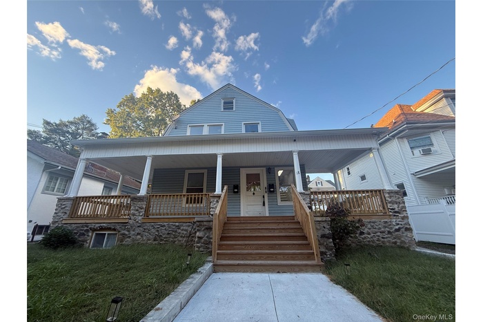 Colonial inspired home with a gambrel roof, covered porch, and a front yard