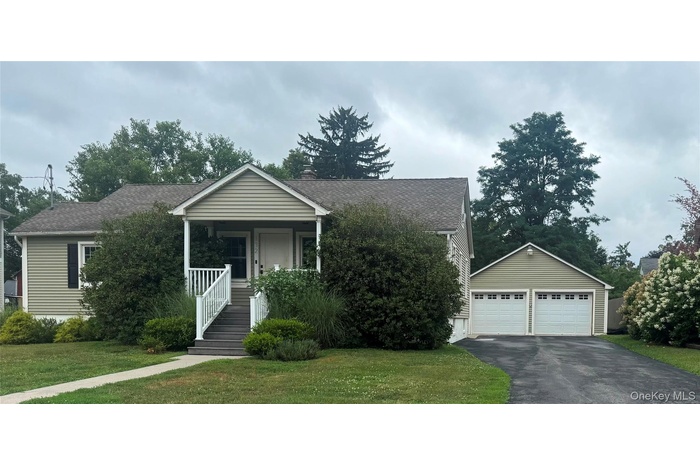 View of front of house featuring a front lawn, a shingled roof, an outbuilding, a porch, and a chimney