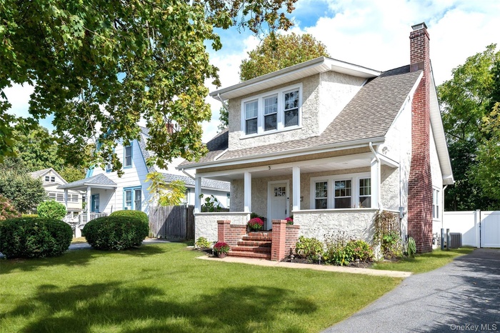 View of front of house with a chimney, a porch, stucco siding, and a shingled roof