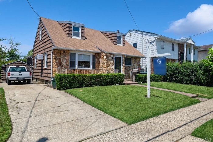 Cape cod house featuring stone siding, a front yard, concrete driveway, and a shingled roof