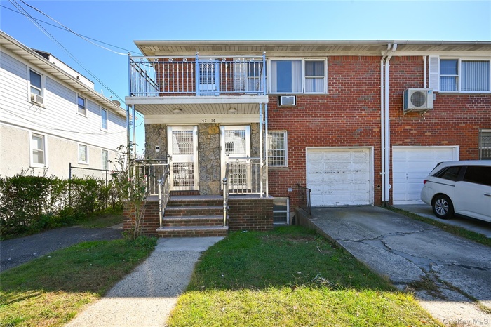 View of front facade featuring concrete driveway, brick siding, an attached garage, and a balcony