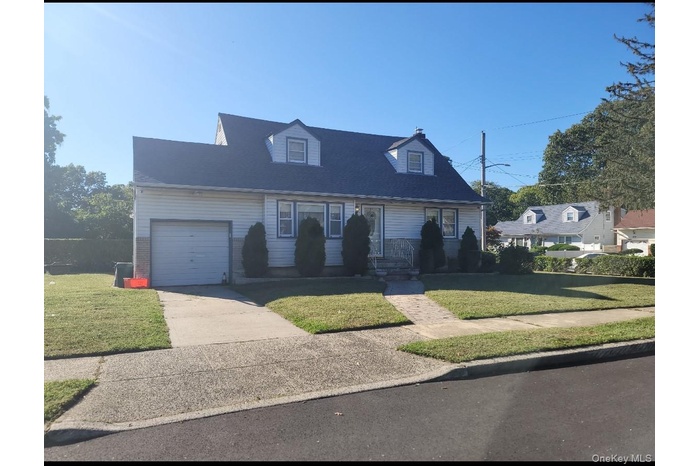 New england style home with a front yard, driveway, brick siding, and an attached garage