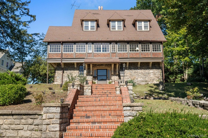 View of front of house featuring stone siding, stairway, a shingled roof, and a front lawn