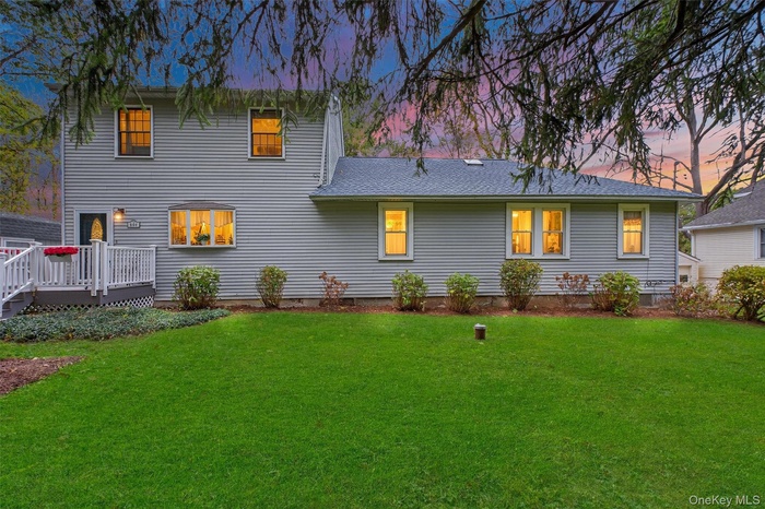 Rear view of property with a lawn, a wooden deck, and roof with shingles