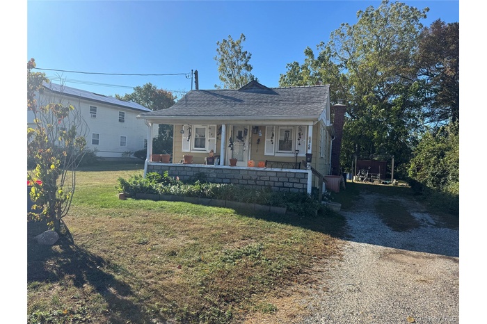 Bungalow-style house with covered porch, a front yard, a shingled roof, and driveway