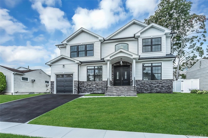View of front facade with stone siding, a front yard, driveway, board and batten siding, and a garage