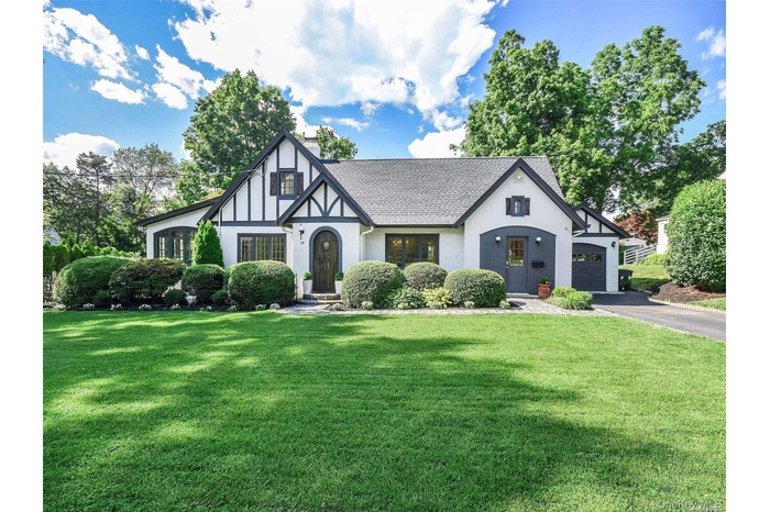 Tudor home featuring a chimney, a front lawn, a shingled roof, stucco siding, and driveway