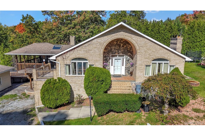 View of front of house with a chimney, brick siding, stone siding, and a wooden deck