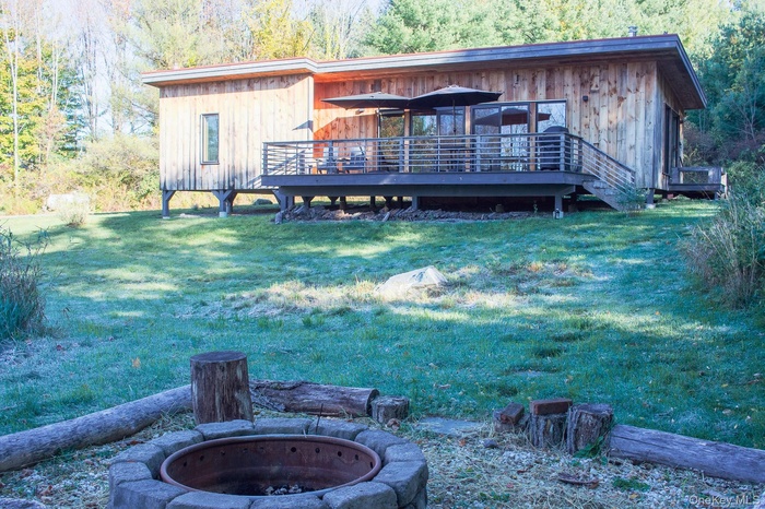 Rear view of property featuring a forest view, a wooden deck, a yard, and an outdoor fire pit